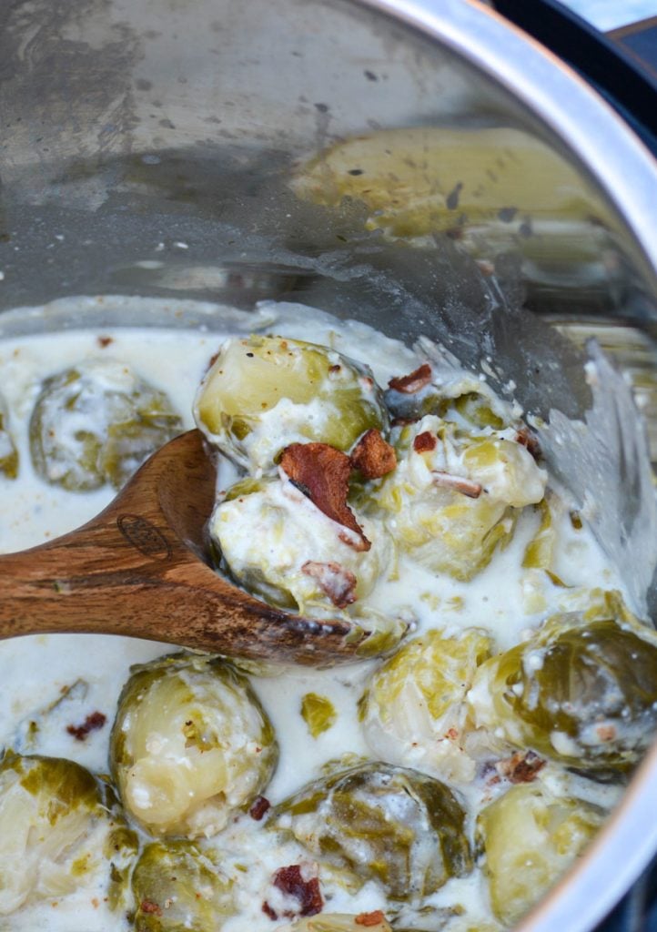 Instant Pot brussels sprouts with bacon shown in the pot with a wooden spoon for serving
