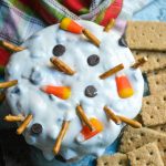 melted snowman dip shown in a black bowl surrounded by graham crackers for dipping