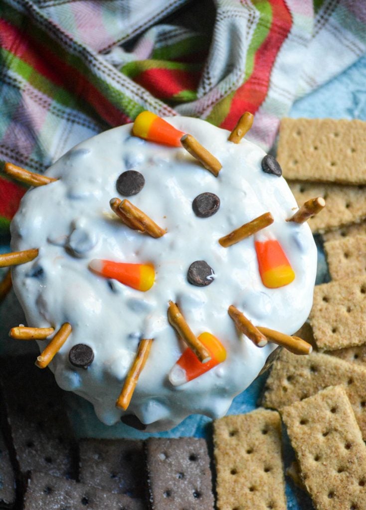 melted snowman dip shown in a black bowl surrounded by graham crackers for dipping