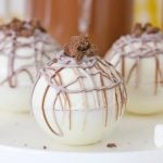 rumchata hot cocoa bombs shown on a white plate with a mug of hot chocolate in the background