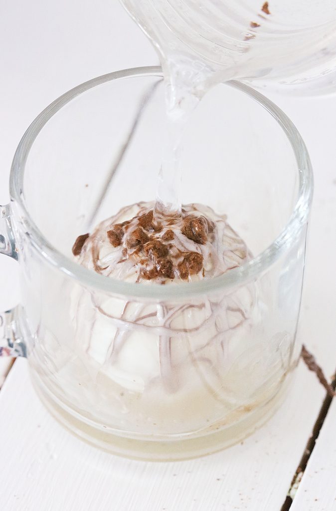 a rumchata hot cocoa bombs shown in a glass mug with hot milk or water being poured over top