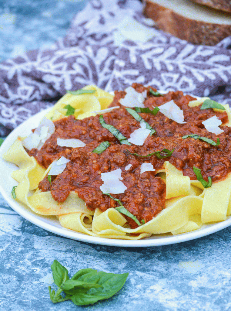 slow cooker bolognese sauce served over a bed of pasta and topped with shaved Parmesan and chiffonade basil leaves 