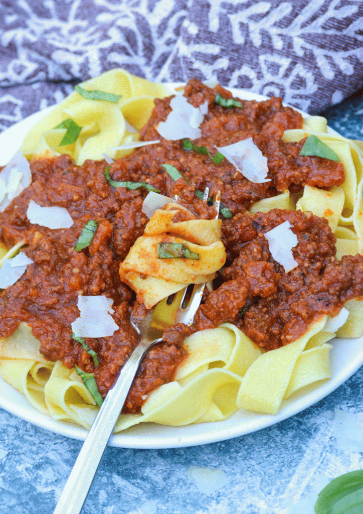 slow cooker bolognese sauce tossed with fresh Italian pasta and swirled with a silver fork on a white plate