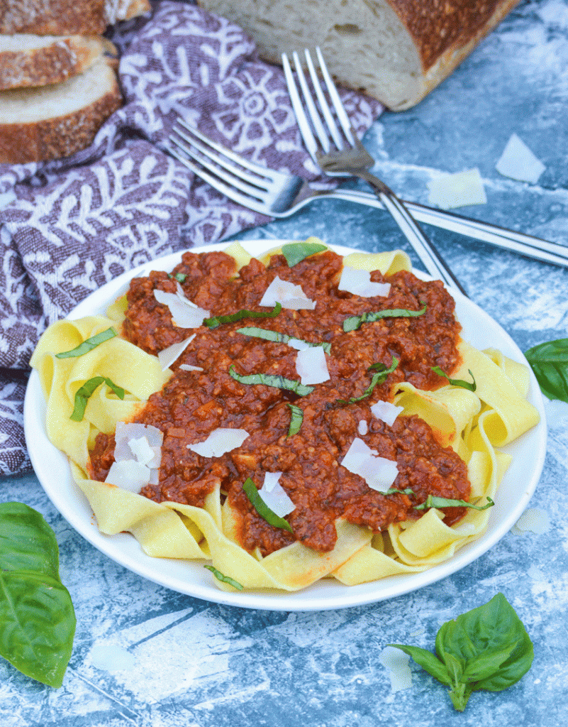 slow cooker bolognese sauce served over a bed of pasta and topped with shaved Parmesan and chiffonade basil leaves