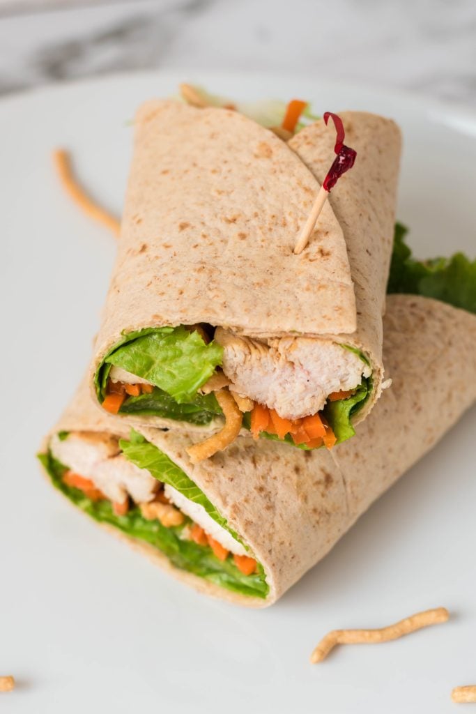 an Asian chicken wrap, cut in half and stacked together on a white plate, secured by tooth picks