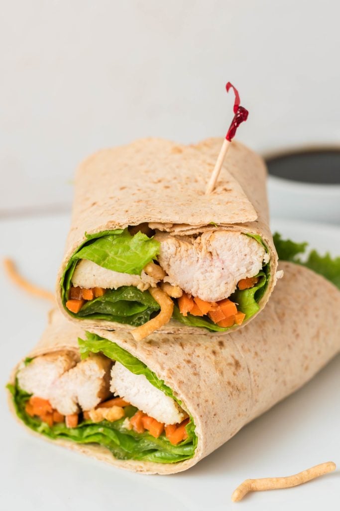 an Asian chicken wrap, cut in half and stacked together on a white plate, secured by tooth picks