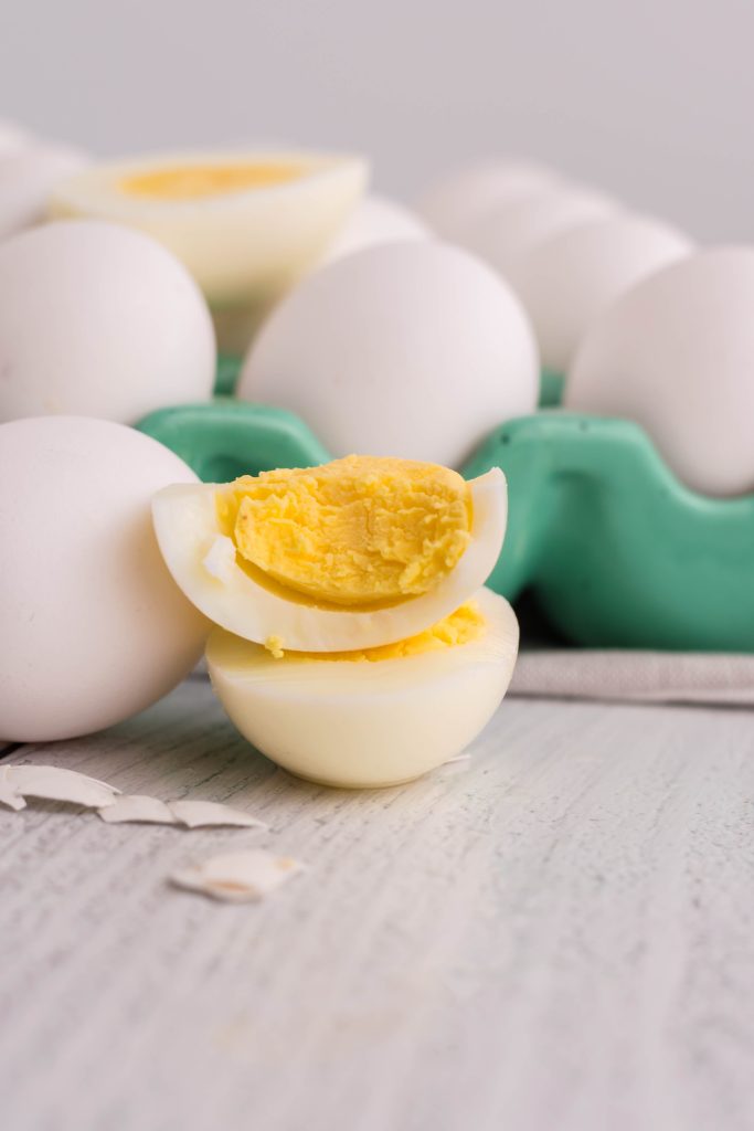 air fryer hard boiled eggs shown cooked and cut in half to reveal the solid yolk center on top of a bed of fresh eggs