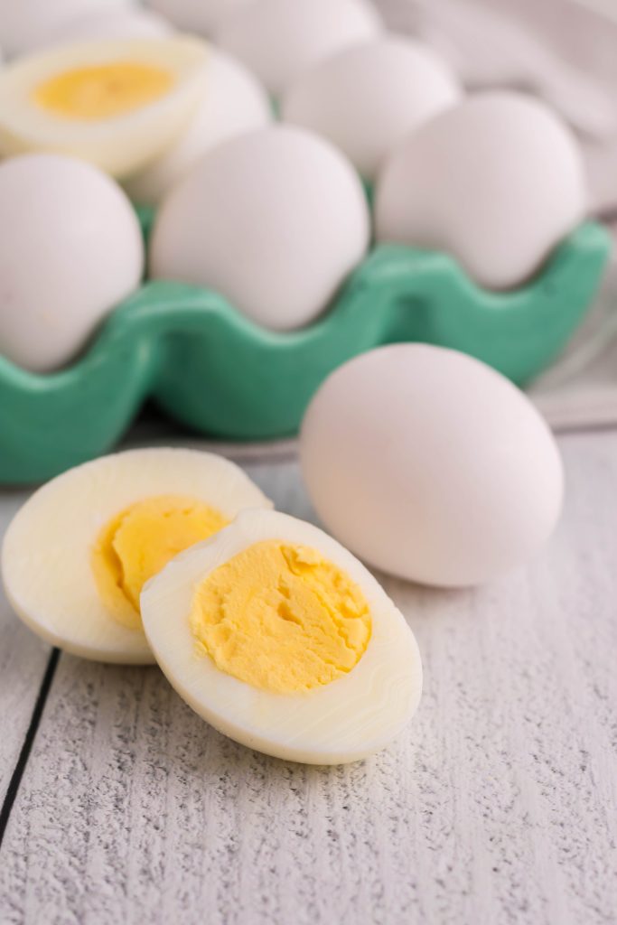 air fryer hard boiled eggs shown cooked and cut in half to reveal the solid yolk center on top of a bed of fresh eggs