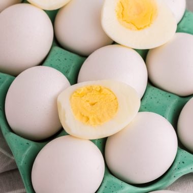 air fryer hard boiled eggs shown cooked and cut in half to reveal the solid yolk center on top of a bed of fresh eggs