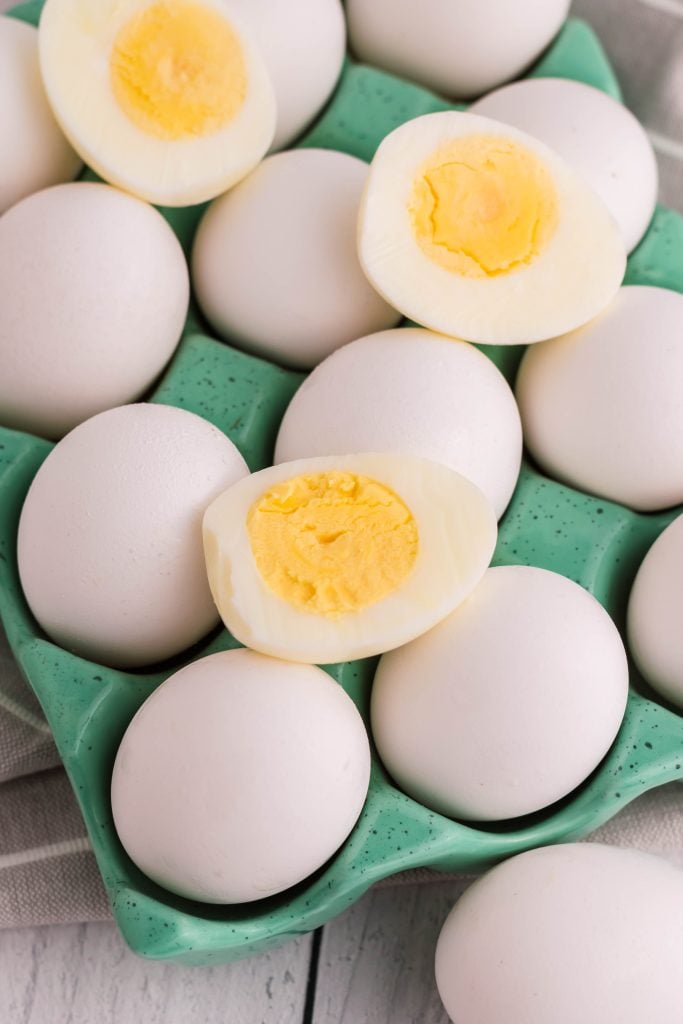 air fryer hard boiled eggs shown cooked and cut in half to reveal the solid yolk center on top of a bed of fresh eggs