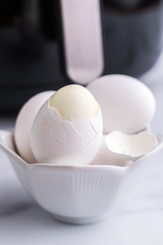 air fryer hard boiled eggs shown being peeled in front on the machine