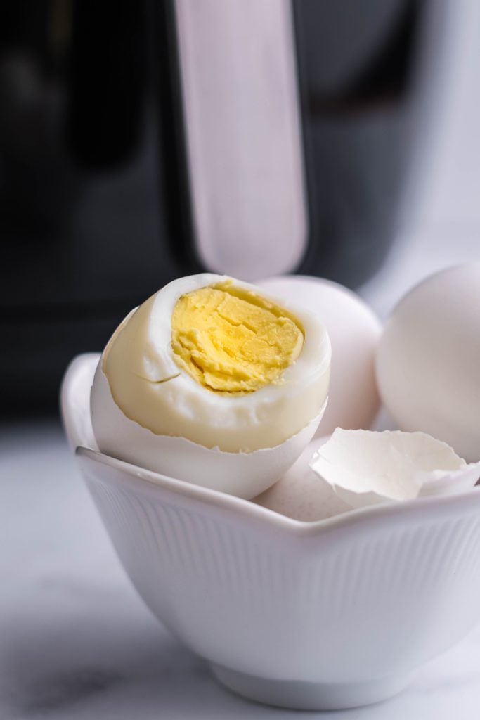 air fryer hard boiled eggs shown being peeled in front on the machine