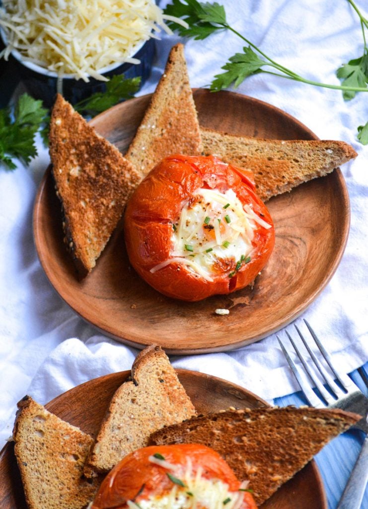 egg stuffed oven roasted tomatoes shown on wooden plates with toast triangles