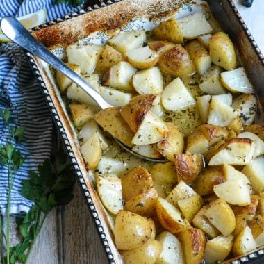 Greek lemon baked potatoes shown in a black & white casserole dish with a silver spoon for serving