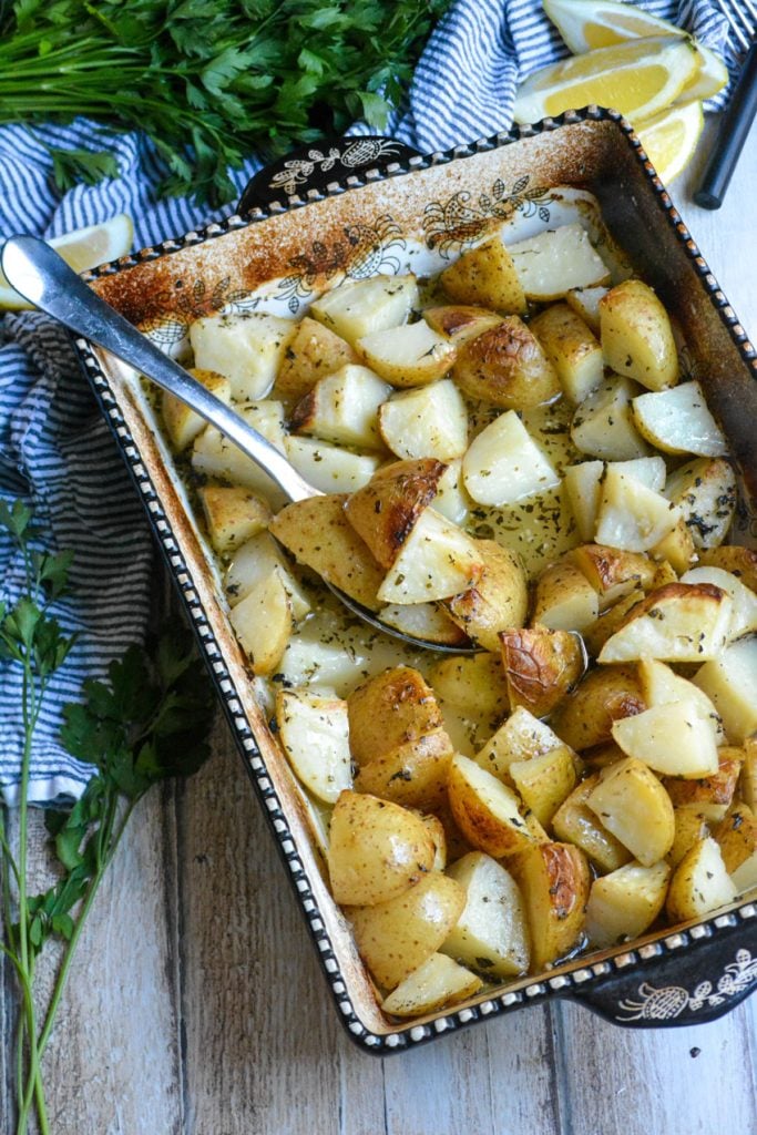Greek lemon baked potatoes shown in a black & white casserole dish with a silver spoon for serving