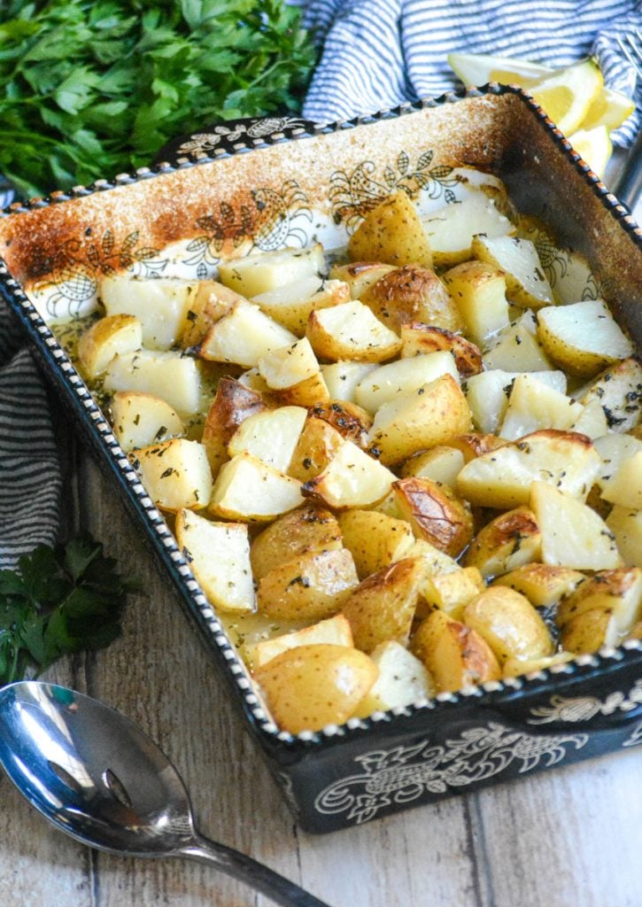 Greek Ellinikos Lemoni Patatas shown baked in a black & white casserole dish with lemon flavored broth