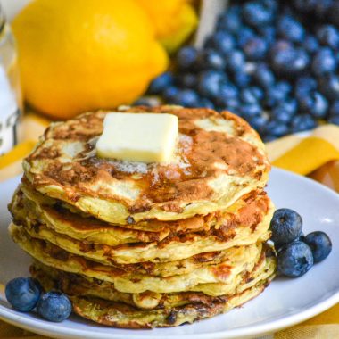 a stack of fluffy cottage cheese pancakes topped with a pat of butter, drizzle of syrup, and serve on a white plate