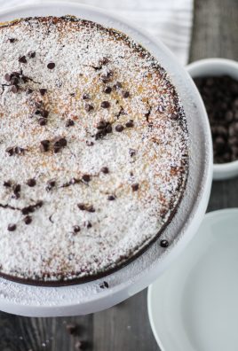 a powdered sugar sprinkled chocolate chip ricotta cake shown on a white cake plate