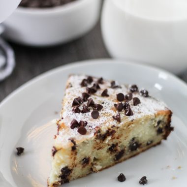 a slice of Italian ricotta cake shown on a white plate and sprinkled with miniature chocolate chips