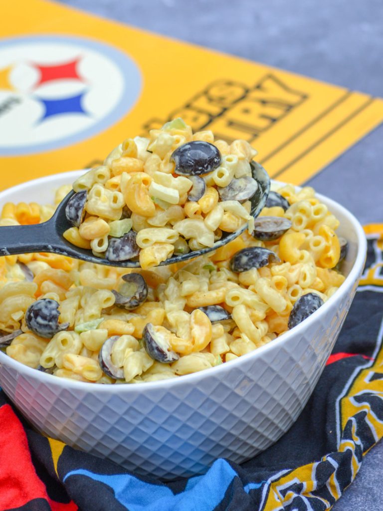 a black serving spoon holding aloft a scoop of pittsburgh steelers pasta salad