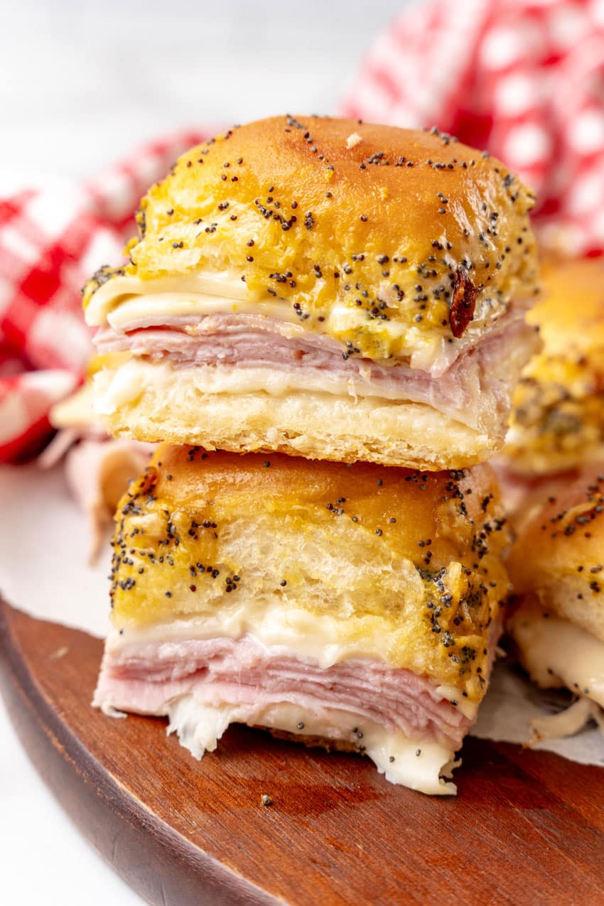 two hot ham and cheese sliders stacked together resting on a wooden cutting board