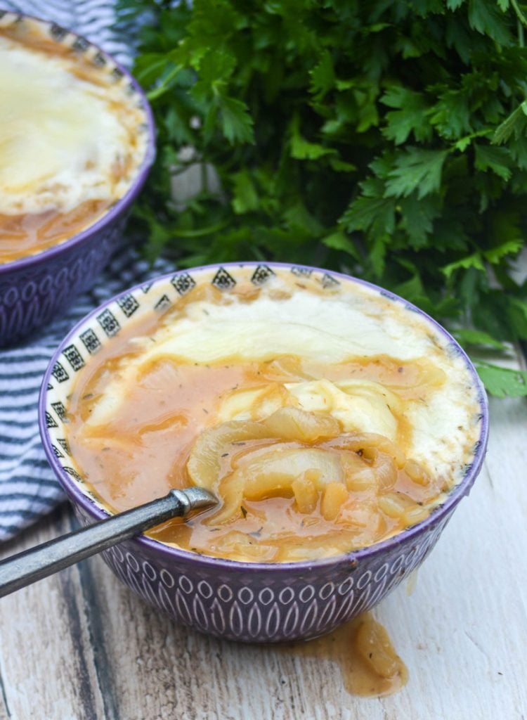 a classic bistro style french onion soup served in a bowl with a spoon and topped with a layer of melted cheese