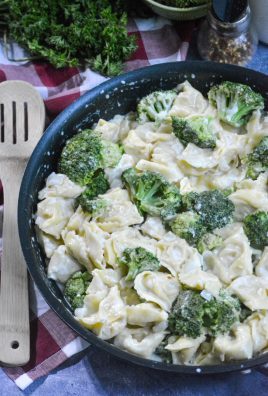 creamy alfredo tortellini with broccoli in a black skillet with a wooden spoon on the side for serving