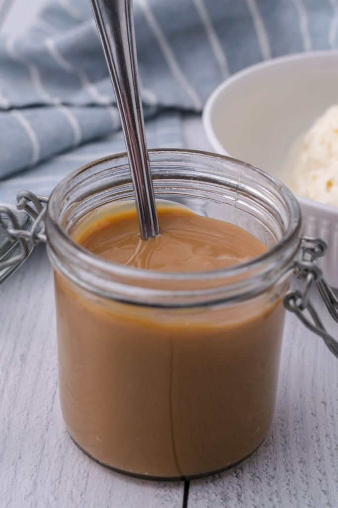 a silver spoon shown sticking out of a glass jar filled with dulce de leche
