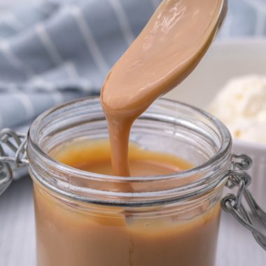 a spoon dripping instant pot dulce de leche into a glass jar