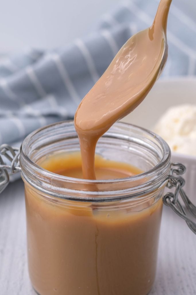 a spoon dripping instant pot dulce de leche into a glass jar