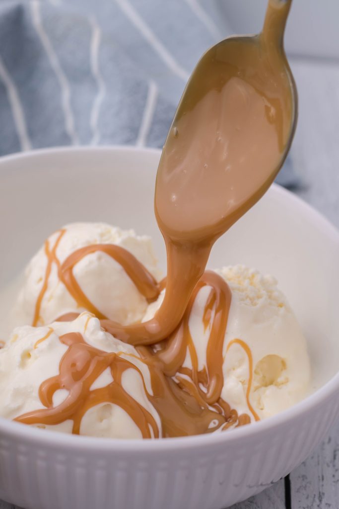 a spoon drizzling Instant pot dulce de leche out over a bowl of vanilla ice cream