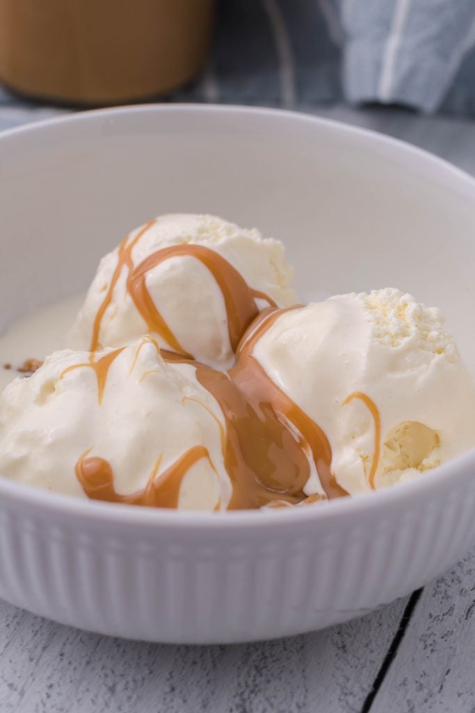 Instant pot dulce de leche poured over vanilla ice cream in a white bowl