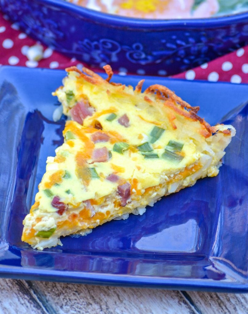 slice of ham and cheese hash brown crusted quiche on a blue square plate