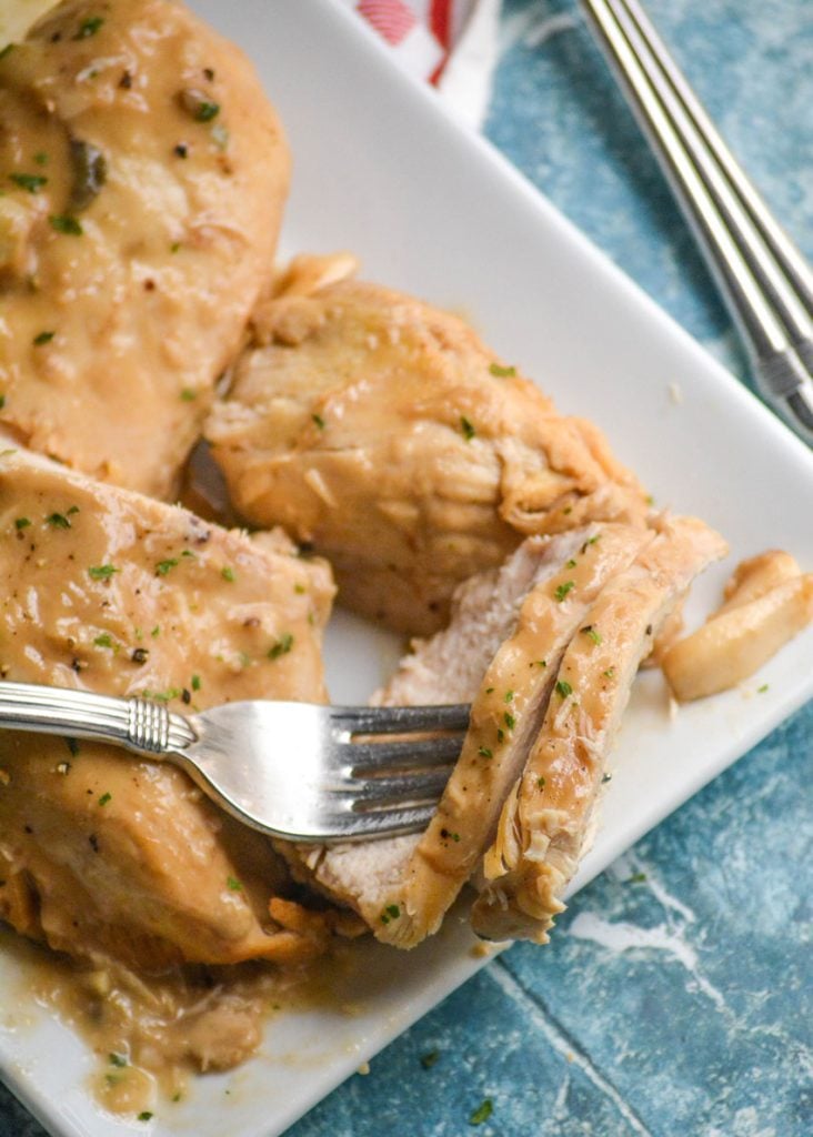a silver fork shown with several slices of Instant Pot 40 cloves of garlic chicken