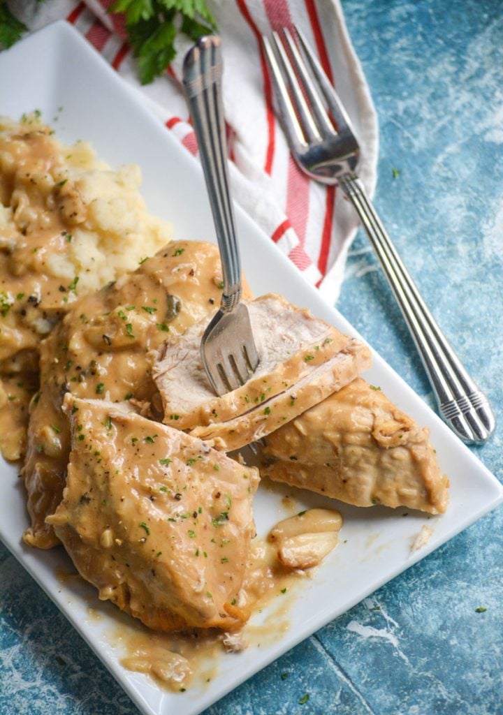 sliced Instant Pot 40 cloves of garlic chicken being pierced with a fork on a white platter