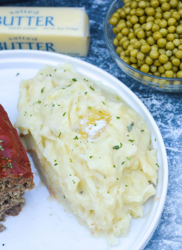 whipped Instant pot mashed potatoes shown on a white plate, topped with a melting pat of butter