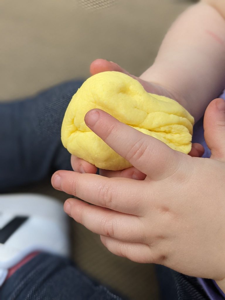 a yellow colored ball of peeps playdough shown in held in two little toddler hands