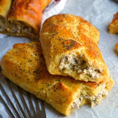 a classic sausage roll shown on a piece of parchment paper and broken open to reveal the creamy sausage filling inside