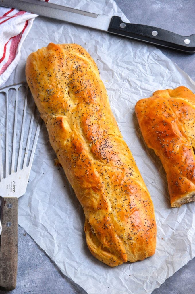classic sausage roll recipe's golden brown log shown on a piece of wrinkled parchment paper