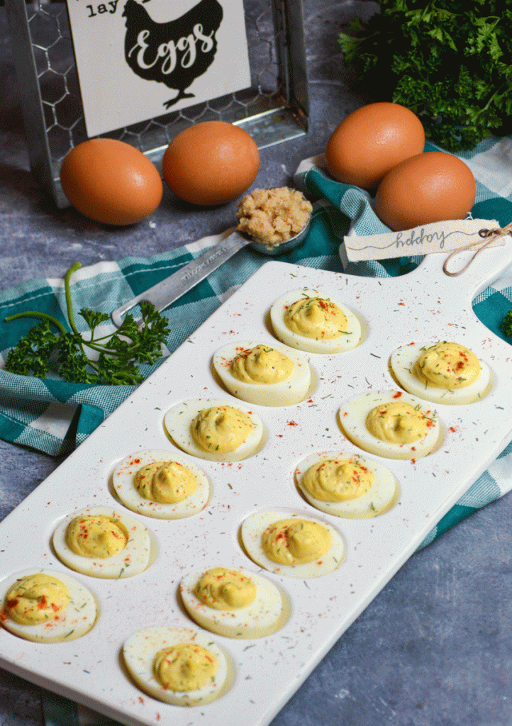 creamy horseradish deviled eggs served on a white egg dish and sprinkled with dried herbs and smoked paprika