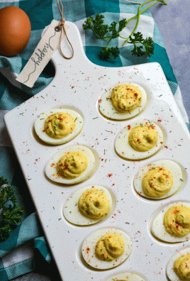 creamy horseradish deviled eggs served on a white egg dish and sprinkled with dried herbs and smoked paprika