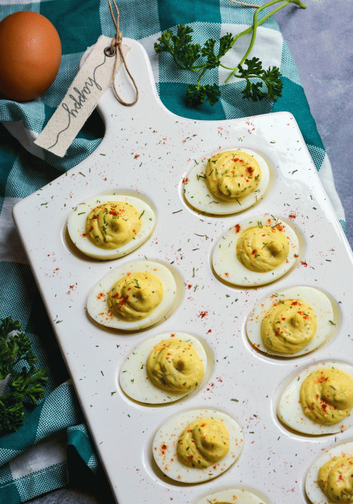 creamy horseradish deviled eggs served on a white egg dish and sprinkled with dried herbs and smoked paprika