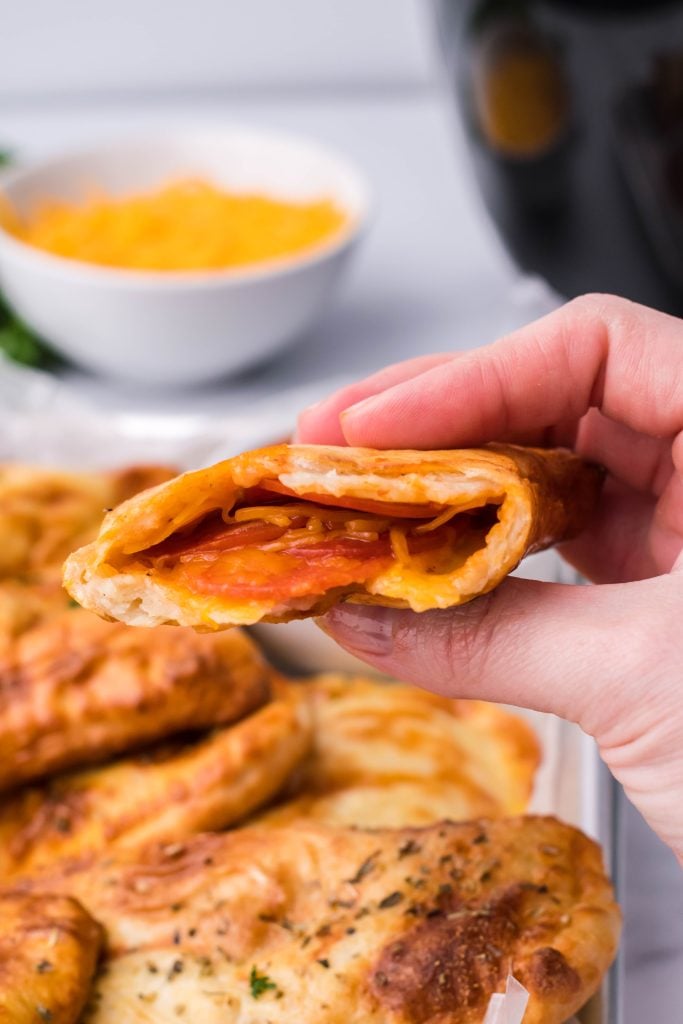 a hand holding up half a air fryer hot pocket to reveal the cheesy pepperoni filling inside