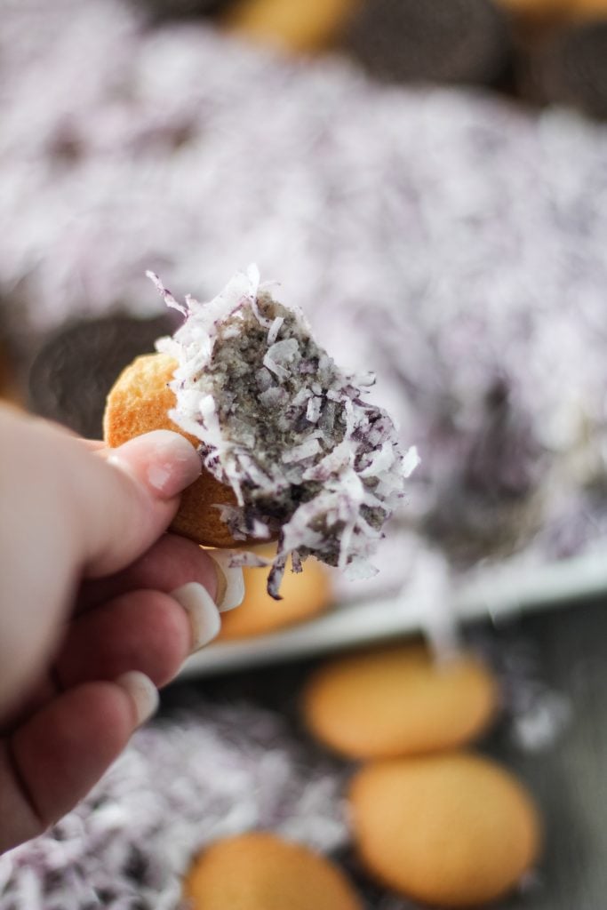 a hand holding up a vanilla wafer topped with cookies and cream cheese ball