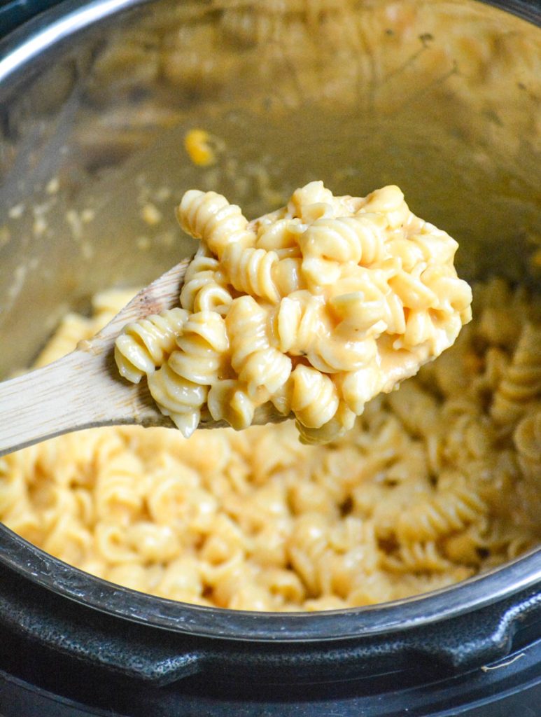 a wooden spoon holding up a scoop of creamy Instant Pot mac and cheese