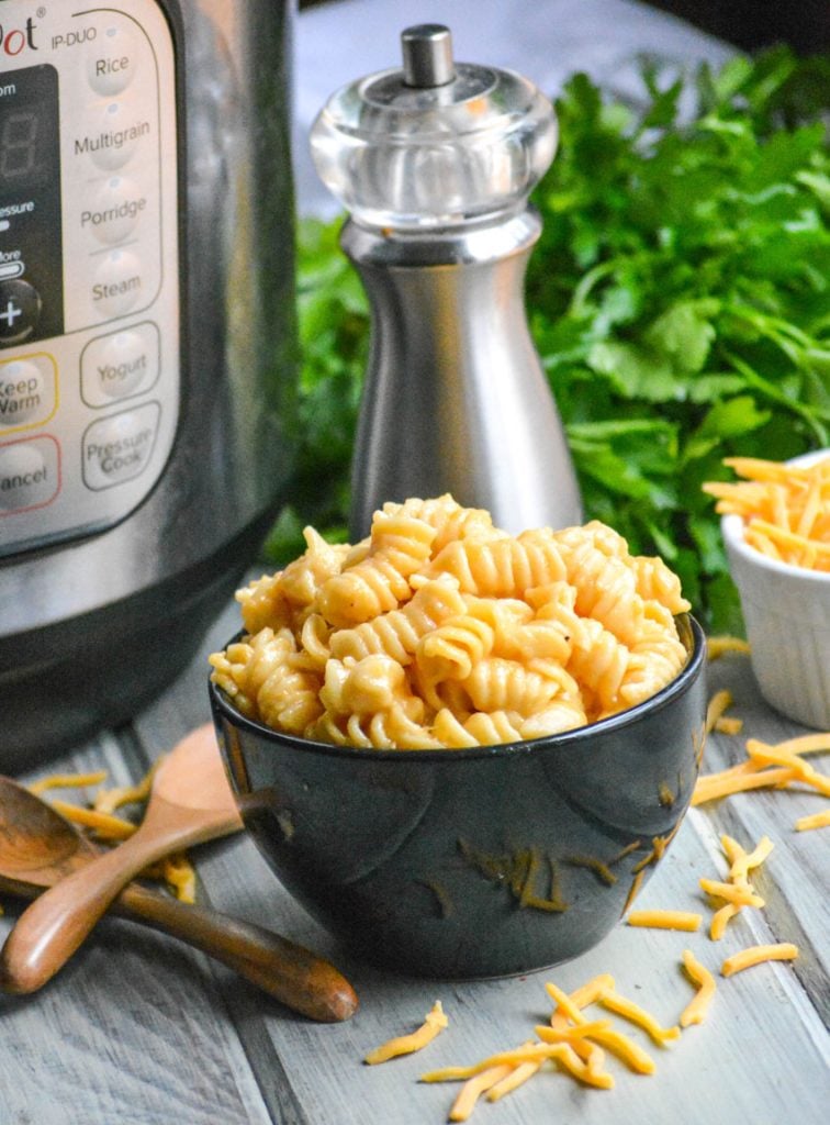 Instant Pot macaroni & cheese shown in a black bowl with wooden spoons on the side for serving
