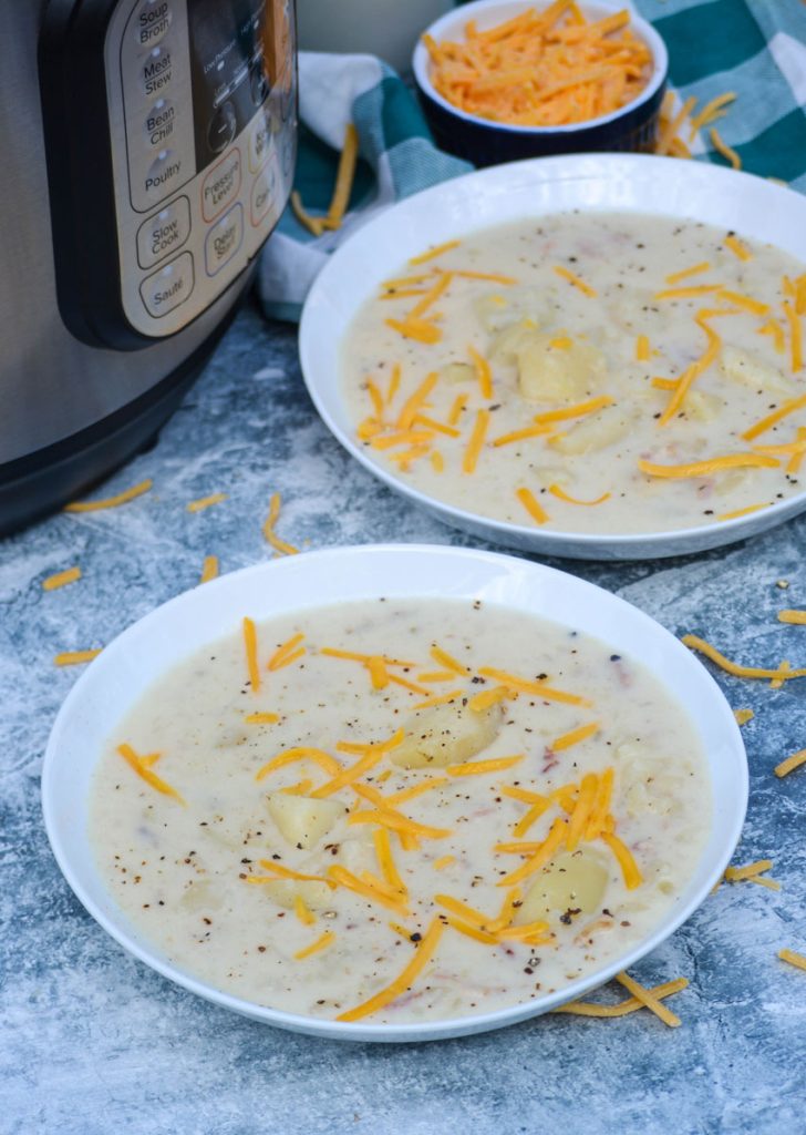 two white bowls filled with classic potato soup in the Instant Pot and topped with cracked pepper and cheddar cheese