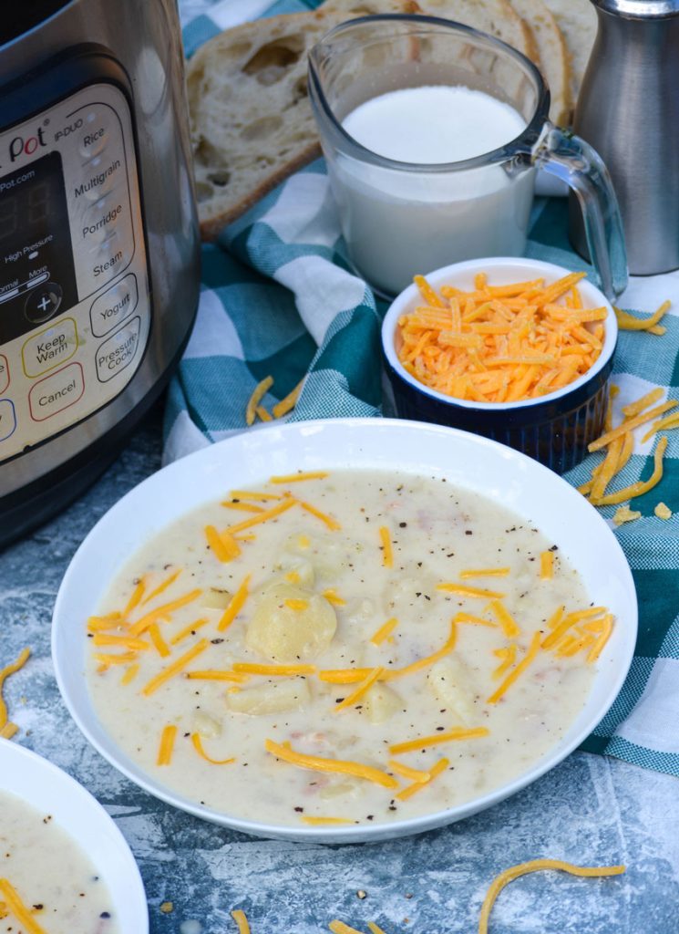 Instant pot potato soup shown in a white bowl and topped with freshly cracked black pepper and shredded cheddar cheese