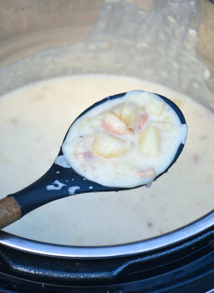 a wooden handled black spoon shown lifting up a scoop of classic potato soup made in the instant pot