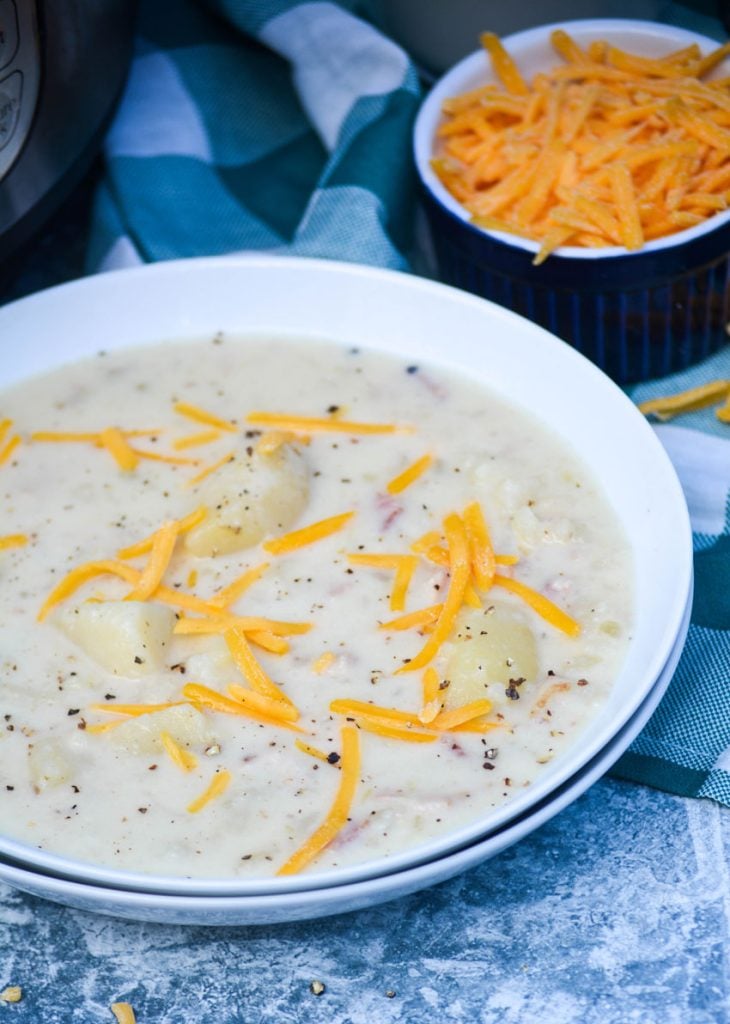 a bowl full of Instant Pot potato soup shown in a white bowl topped with a sprinkle of shredded cheese